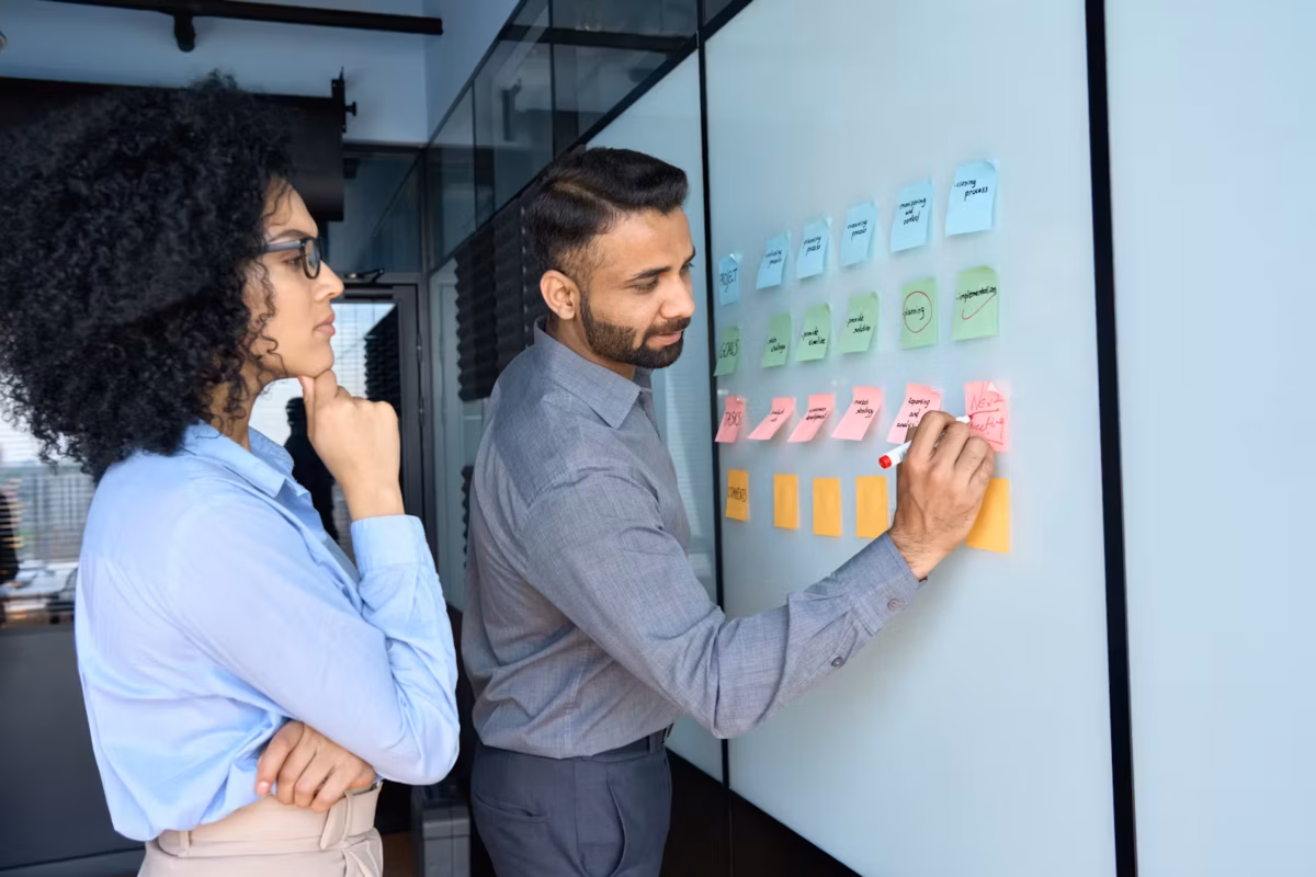 A woman and man writing on sticky notes on a board